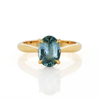 Gold ring with a teal sapphire gemstone on a white background
